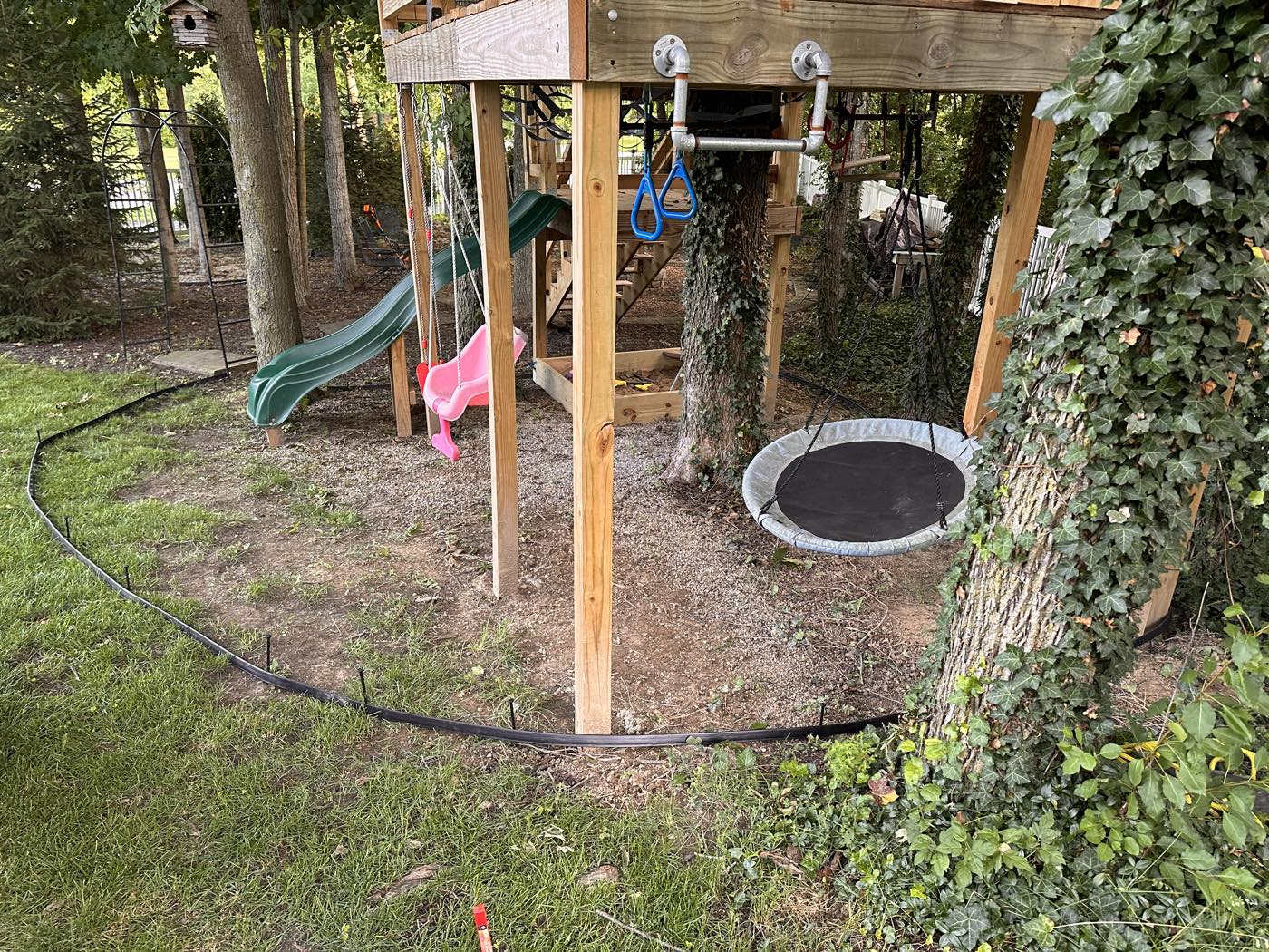 Bare, muddy ground under a backyard playset before gravel install